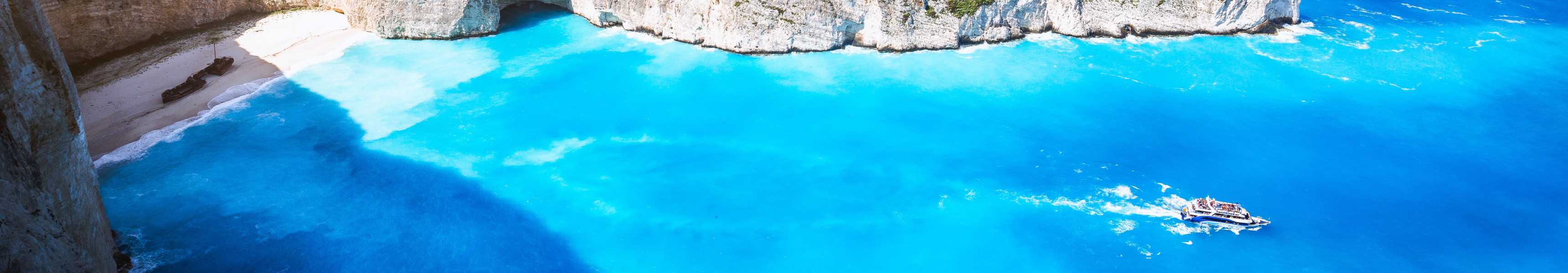 Die ber&uuml;hmte Navagio-Bucht auf Zakynthos in Griechenland mit t&uuml;rkisblauem Wasser, wei&szlig;en Klippen, einem Schiffswrack am Strand und einem Ausflugsboot im Meer.