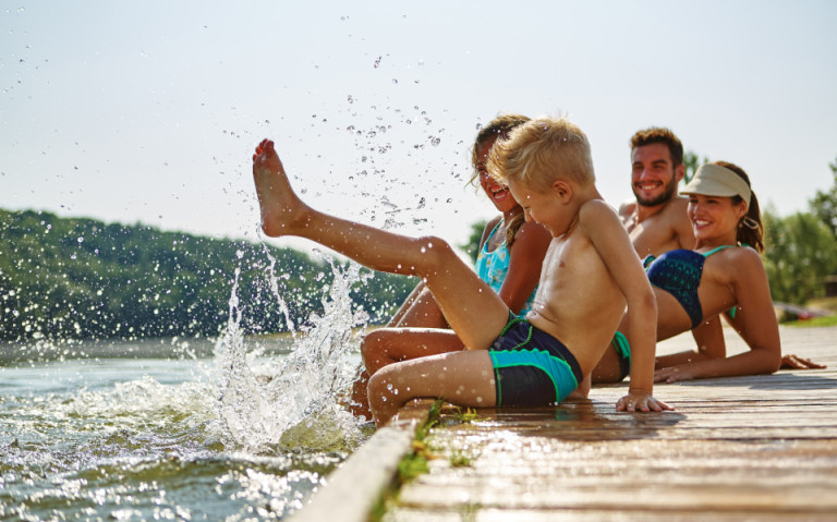 Familie am Gardasee, die am Steg sitzt und mit ihren Füßen im Wasser planscht.