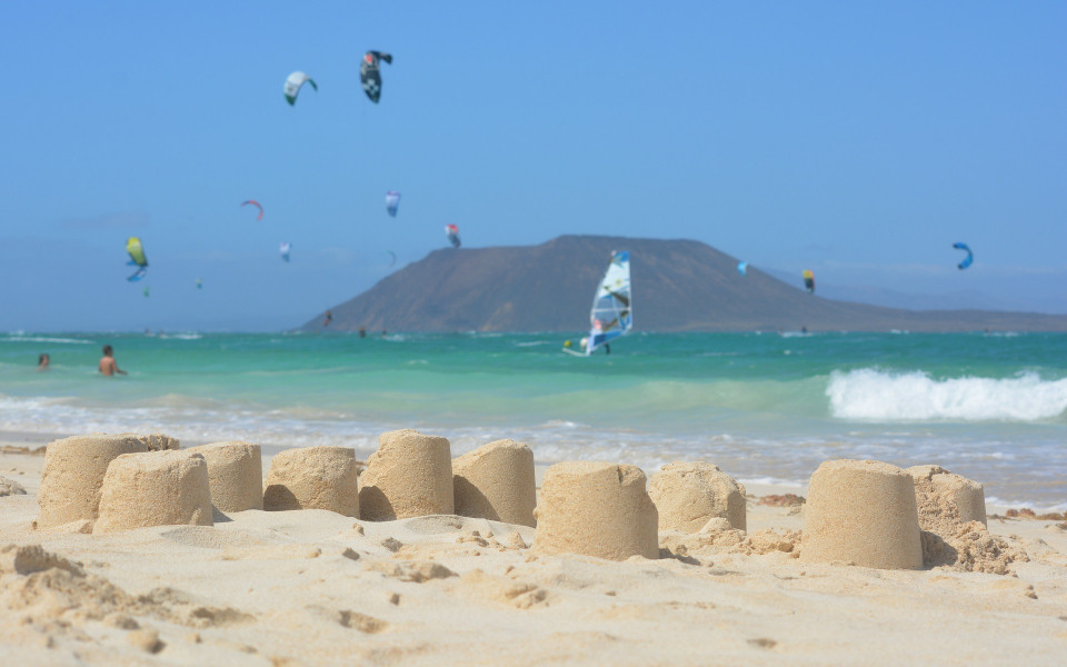 Strand mit Sandburgen und Kite-Surfern im Meer