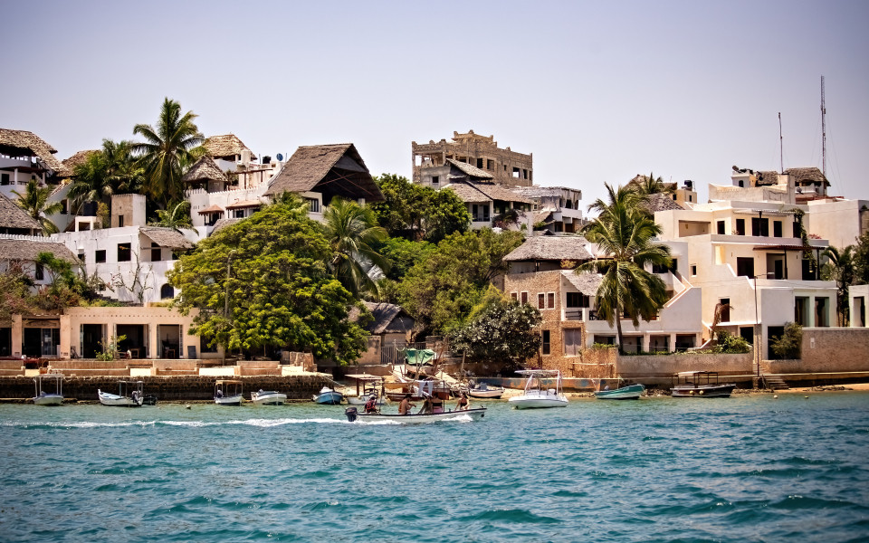 Die Küste von Lamu in Kenia mit traditionellen Häusern und Fischerbooten am Wasser.