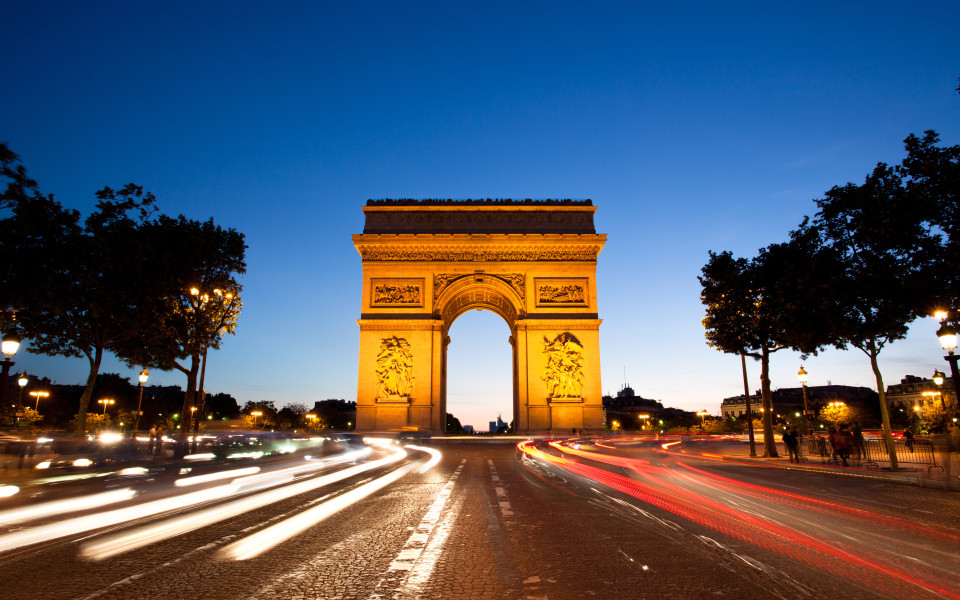 Arc de Triomphe in Paris bei Nacht mit Lichtspuren vorbeifahrender Autos