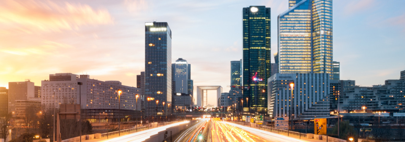 Stadtviertel La Défense in Paris mit modernen Hochhäusern und Lichtspuren des Verkehrs bei Sonnenuntergang
